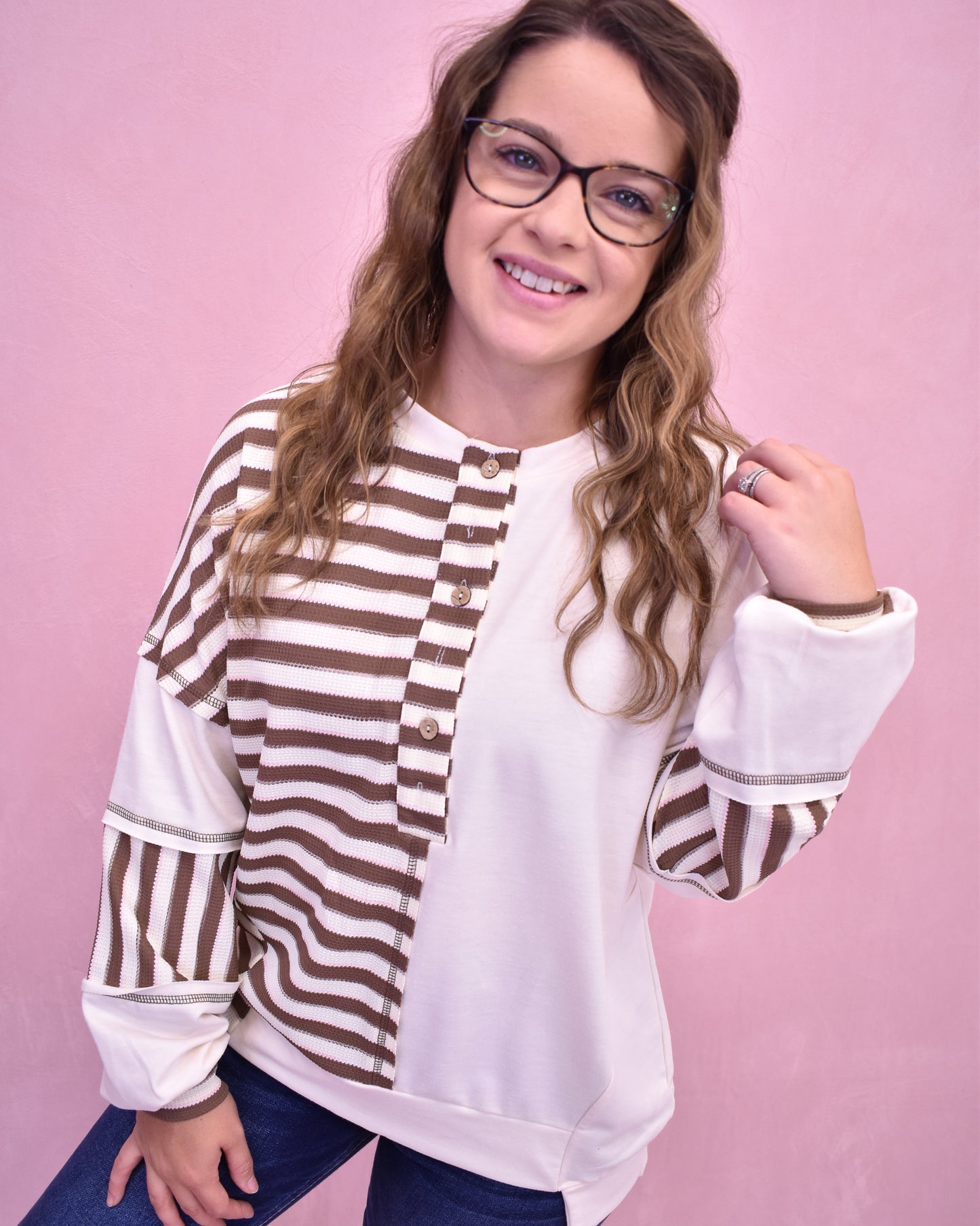 Woman wearing a white blouse with brown striped sleeves against a pink background