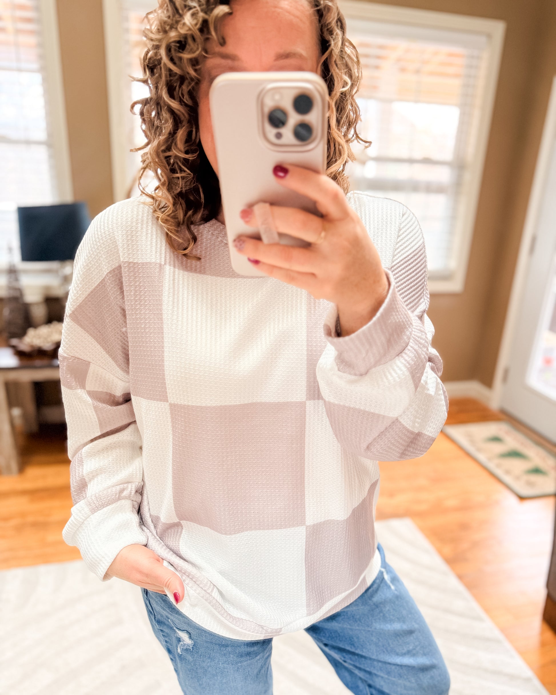 Person wearing a checkered sweater and jeans, taking a mirror selfie.