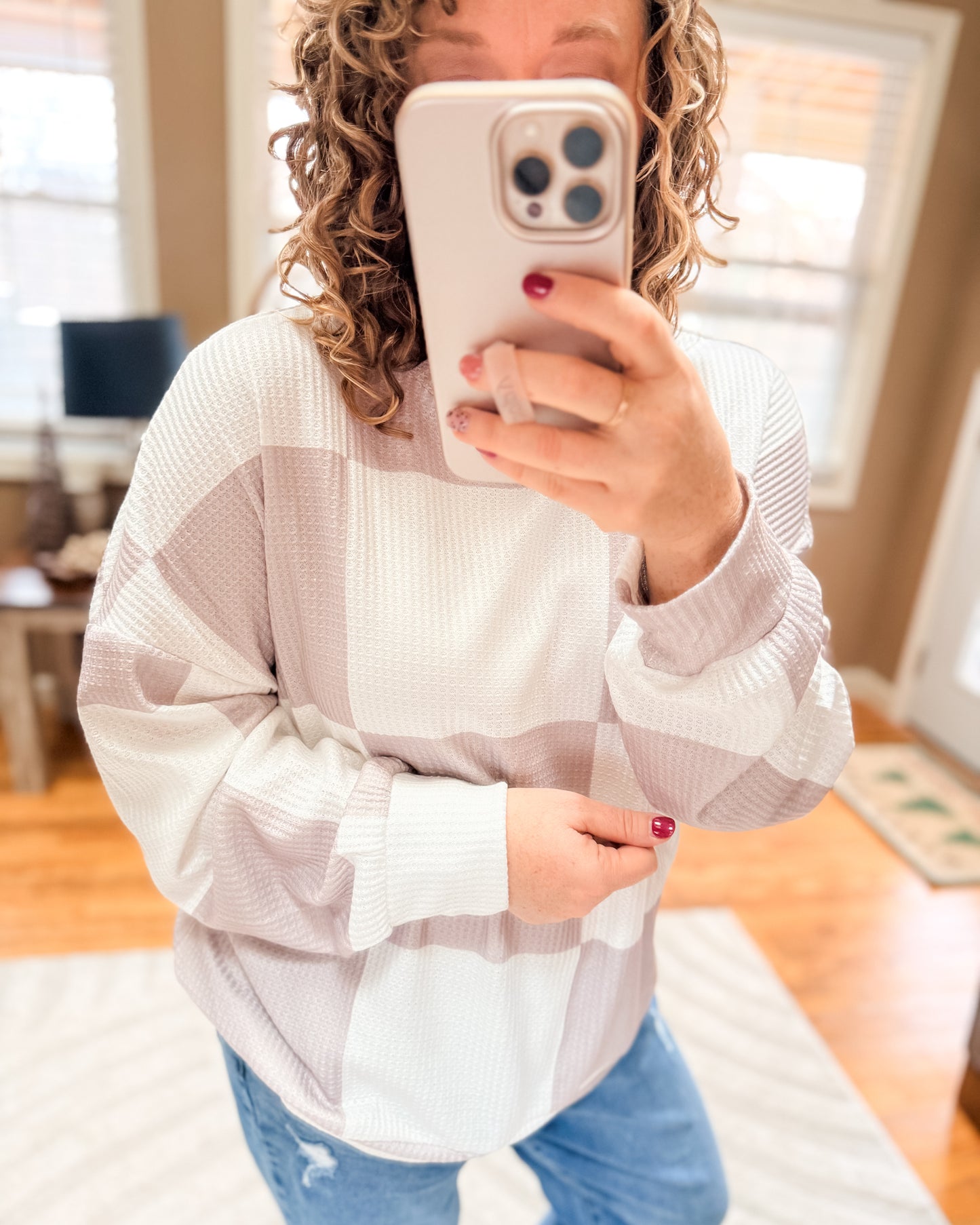 Person taking a mirror selfie wearing a light-colored sweater and blue jeans.