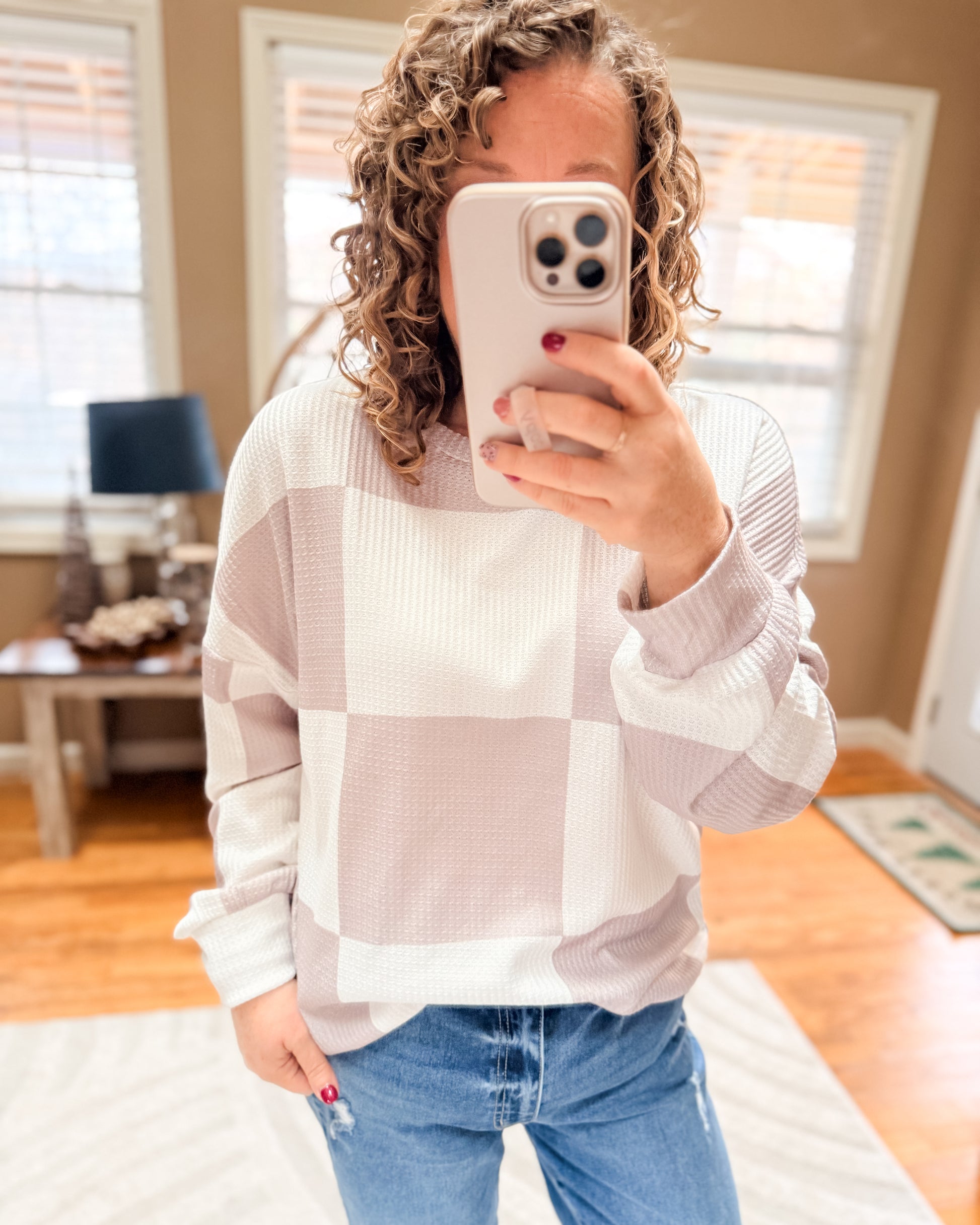 Person wearing a checkered shirt and jeans taking a mirror selfie.