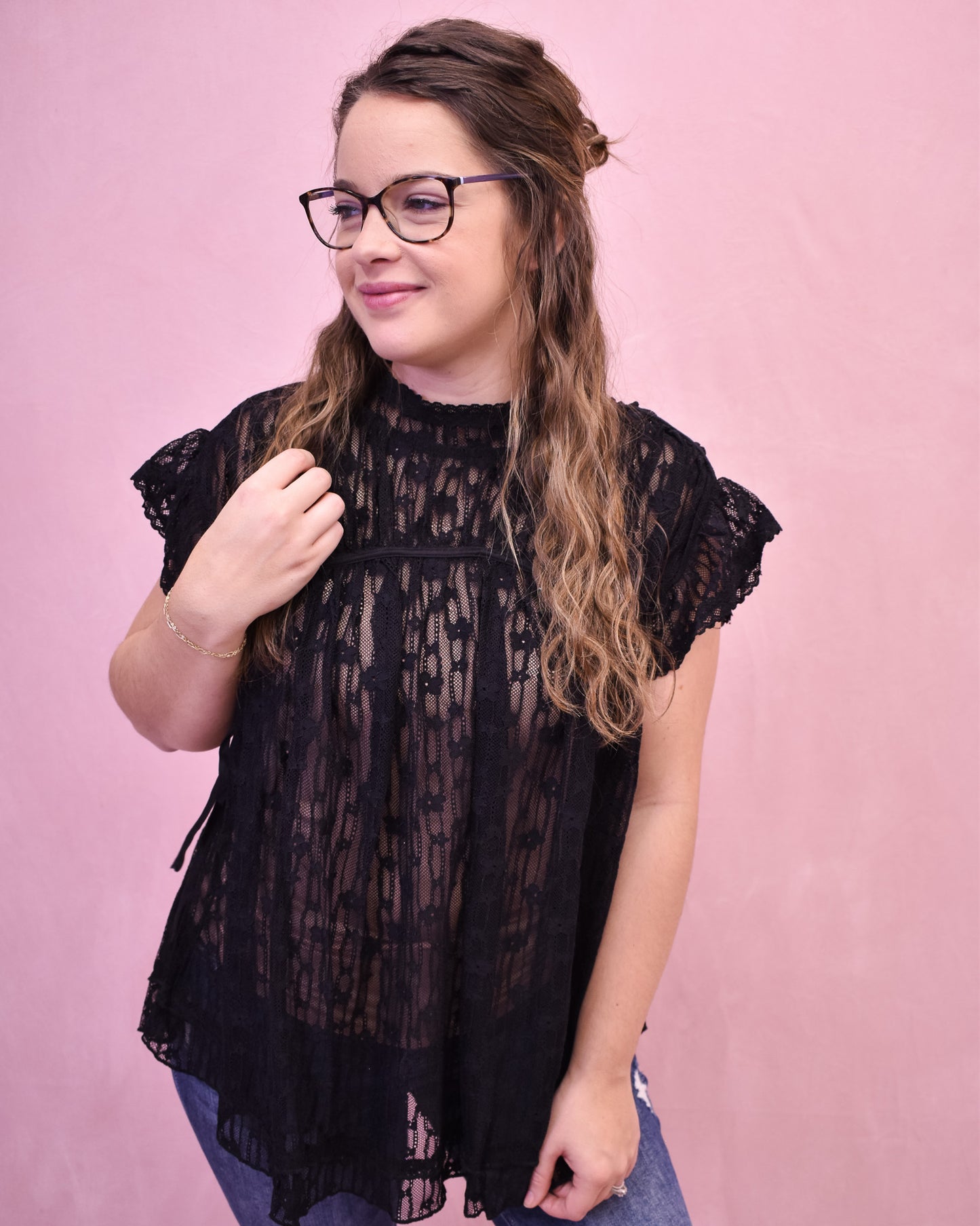 Woman wearing a black lace top against a pink background