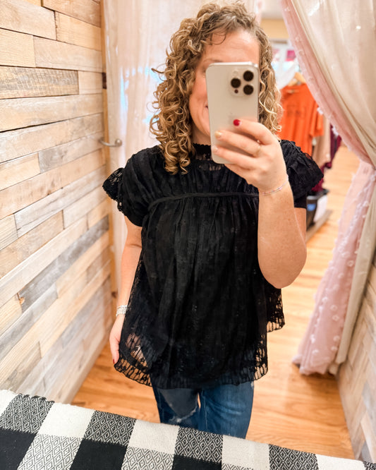 Person wearing a black top taking a mirror selfie in a store.