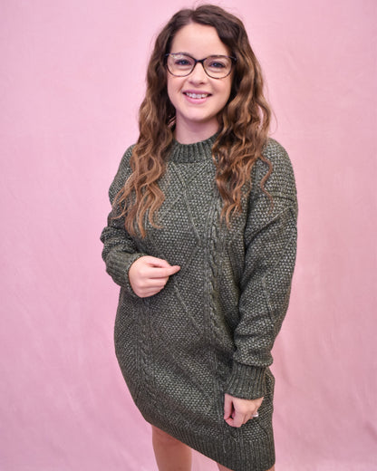 Woman wearing a green knitted sweater dress against a pink background