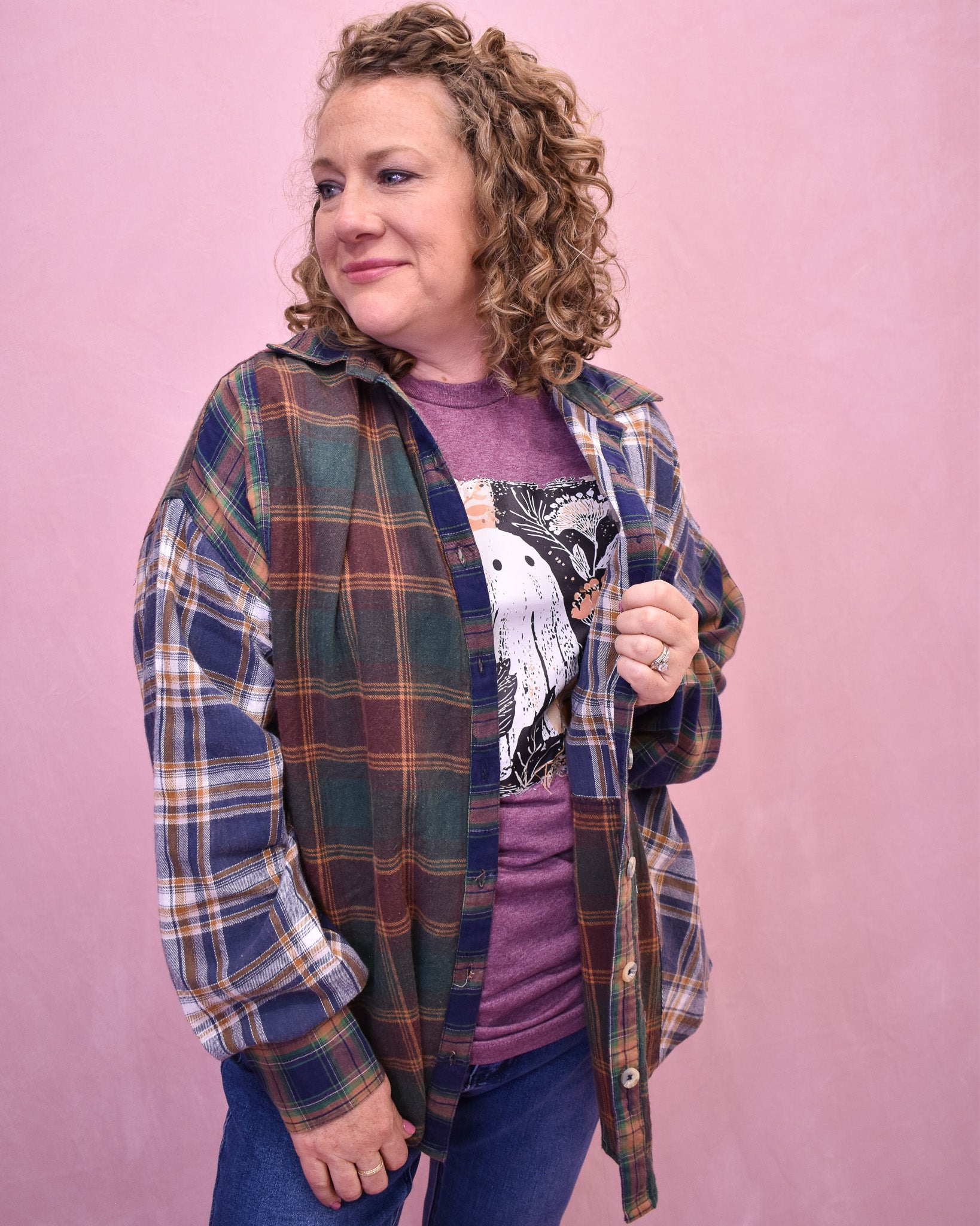 Person wearing a plaid shirt over a graphic t-shirt against a pink background