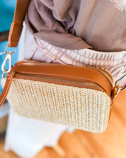 Woven handbag with brown strap worn as a crossbody
