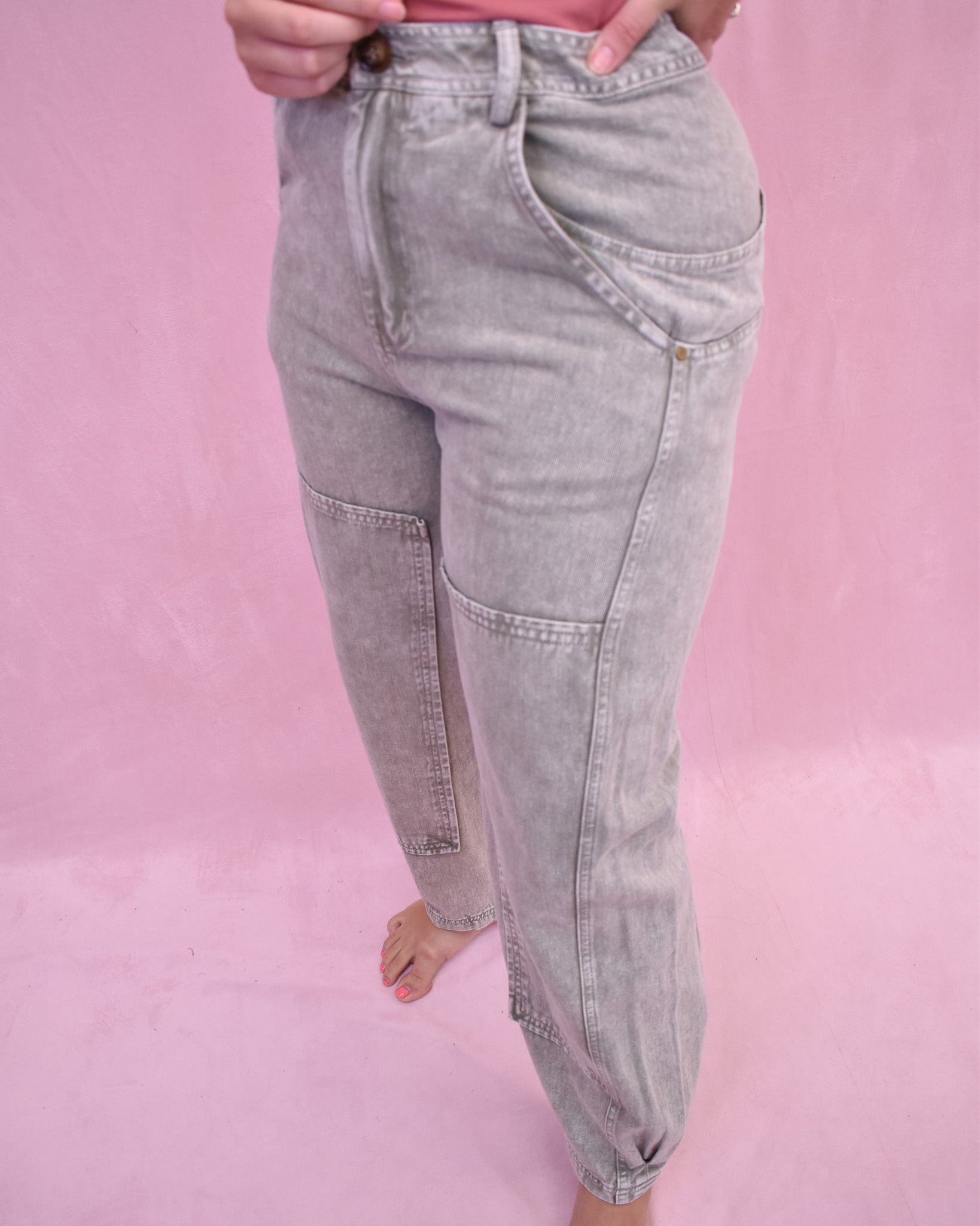 Gray jeans worn by a person on a pink background