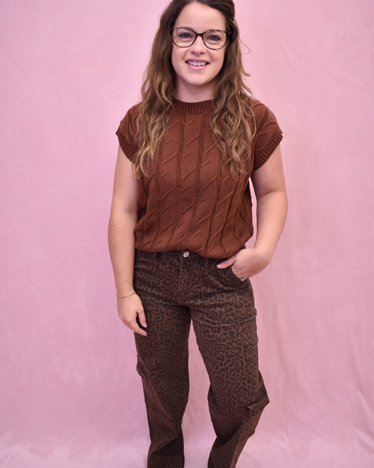 Person wearing a brown cable knit top and leopard print pants against a pink background