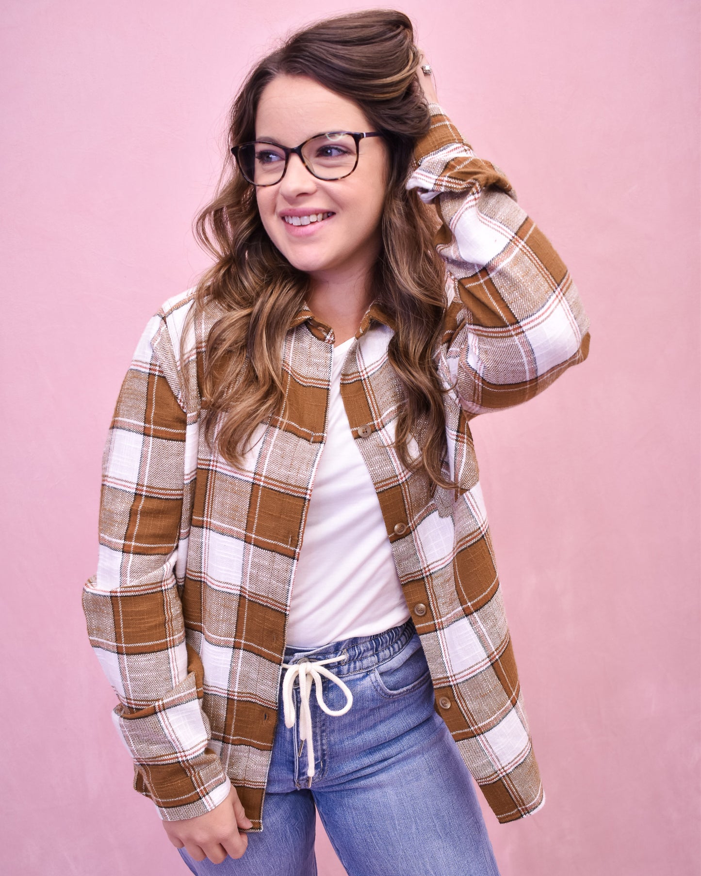 Woman wearing a plaid shirt and jeans against a pink background