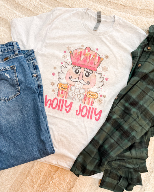 White t-shirt with 'Holly Jolly' design, blue jeans, and green plaid shirt on a beige surface