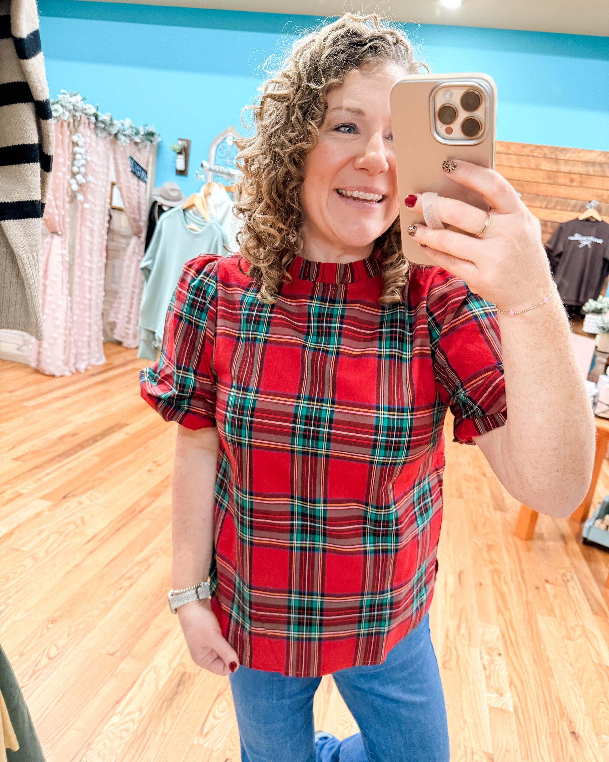 Woman taking a mirror selfie wearing a red plaid shirt in a store.