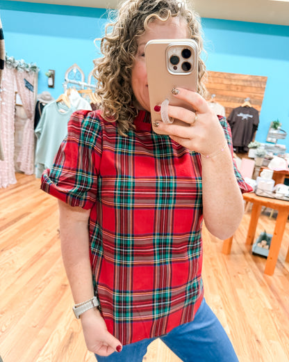 Woman taking a mirror selfie wearing a red plaid shirt in a store.