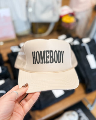 a beige trucker style snapback hat with homebody printed in black 