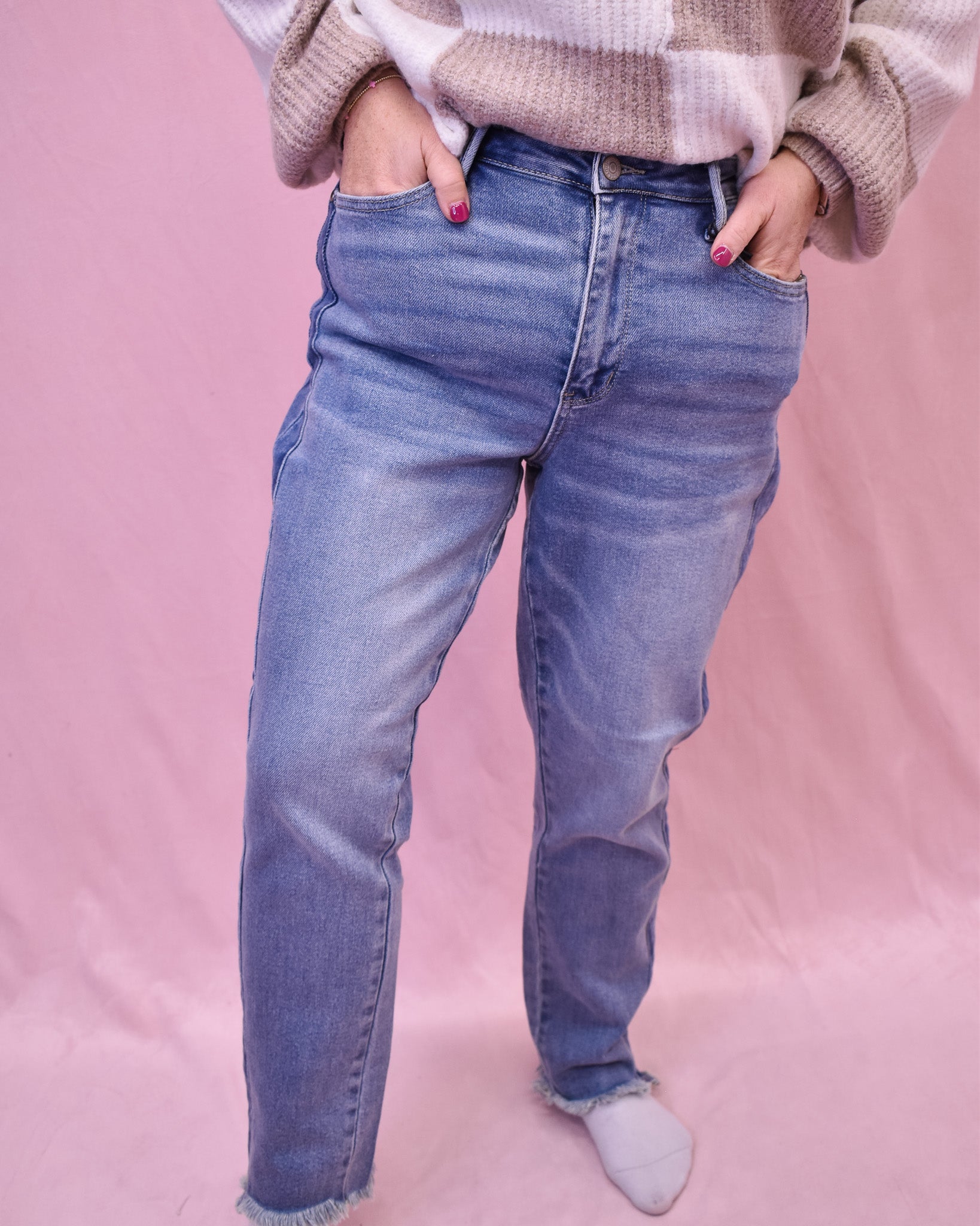 Person wearing blue jeans and a patterned sweater on a pink background