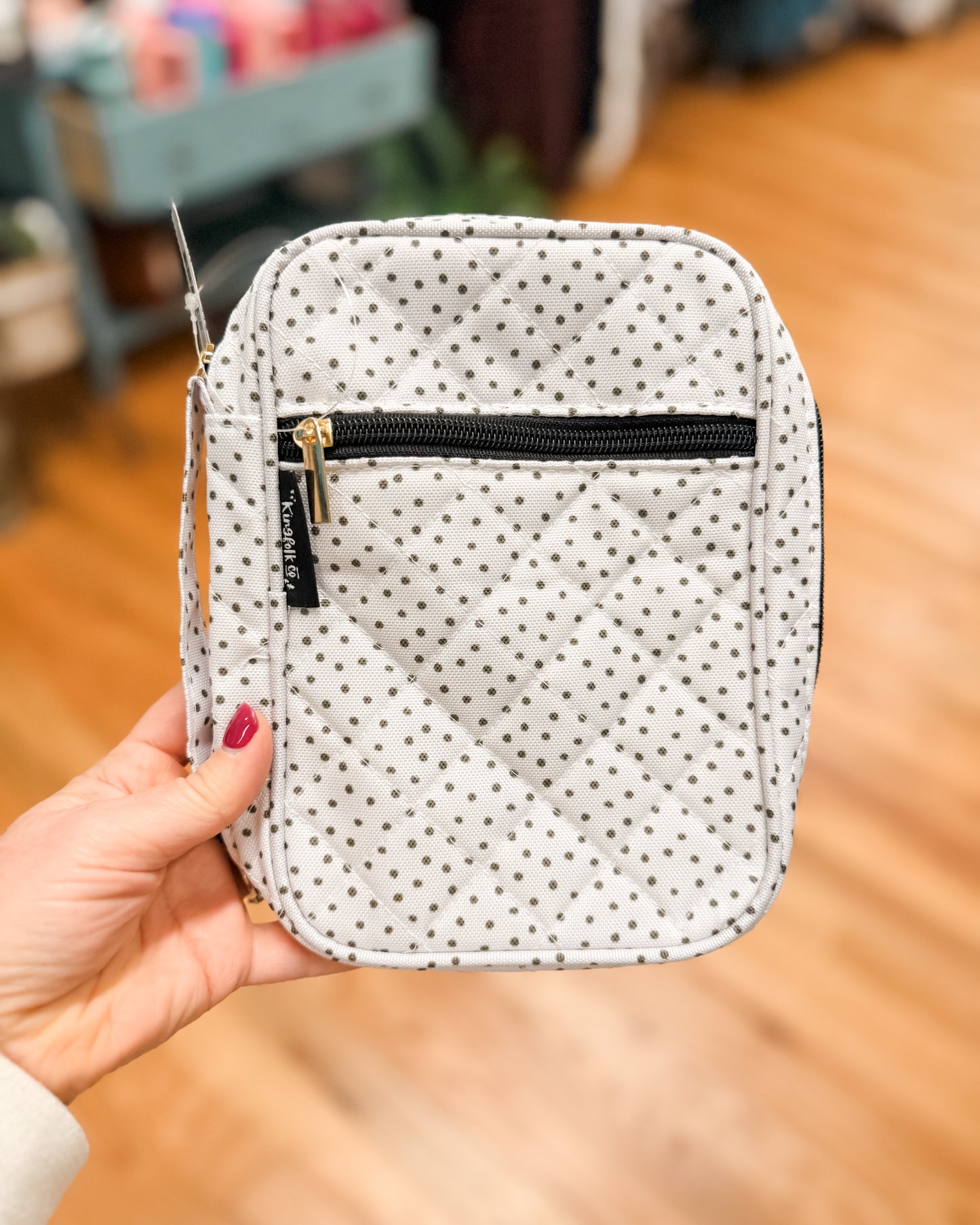 Polka dot pouch with a black zipper held by a hand on a wooden floor.