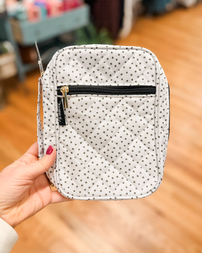 Polka dot pouch with a black zipper held by a hand on a wooden floor.