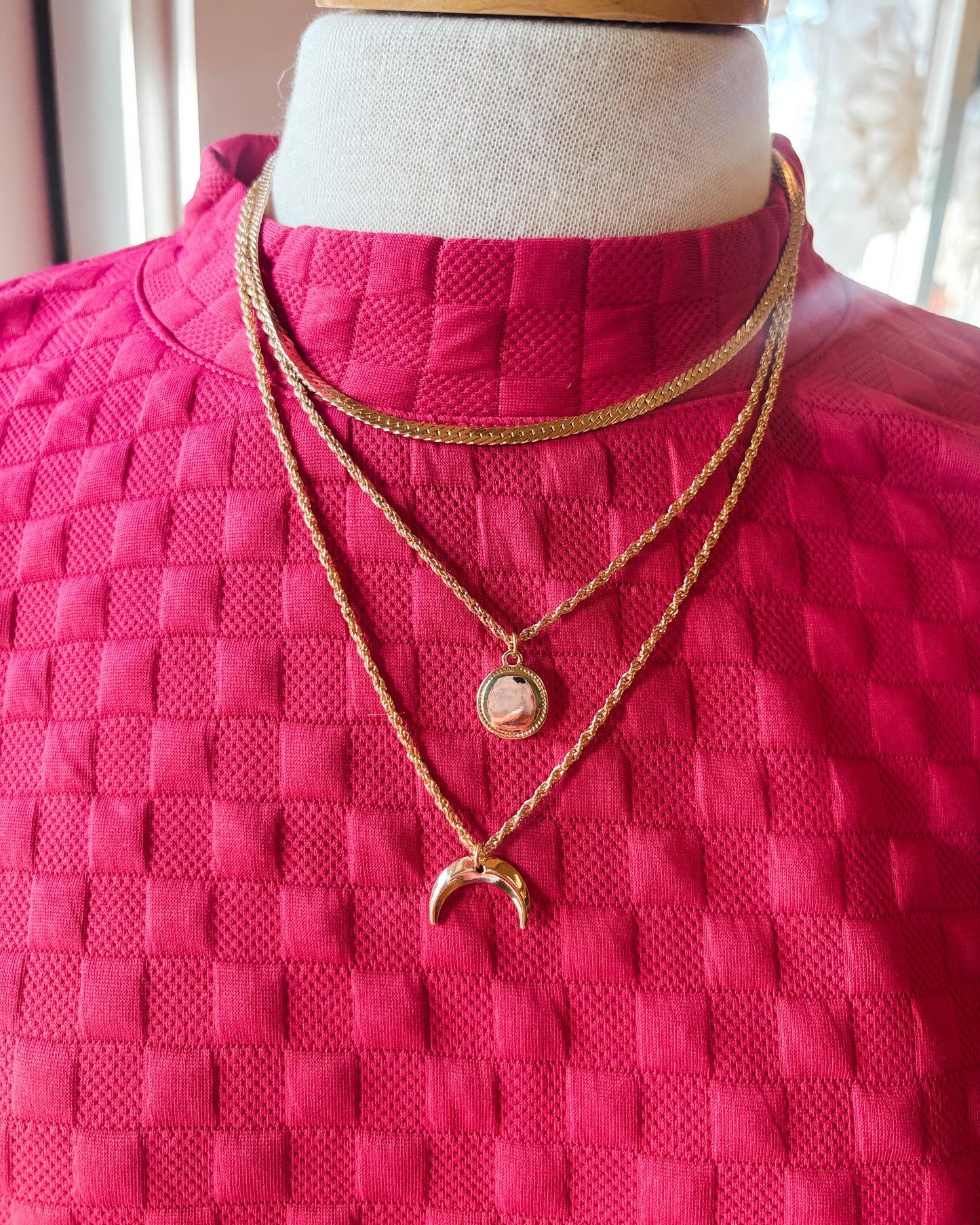 Mannequin wearing a bright pink textured garment with gold necklaces.