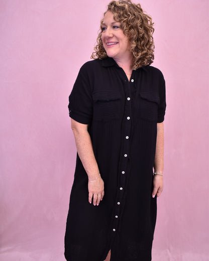 Woman wearing a black dress with white buttons against a pink background