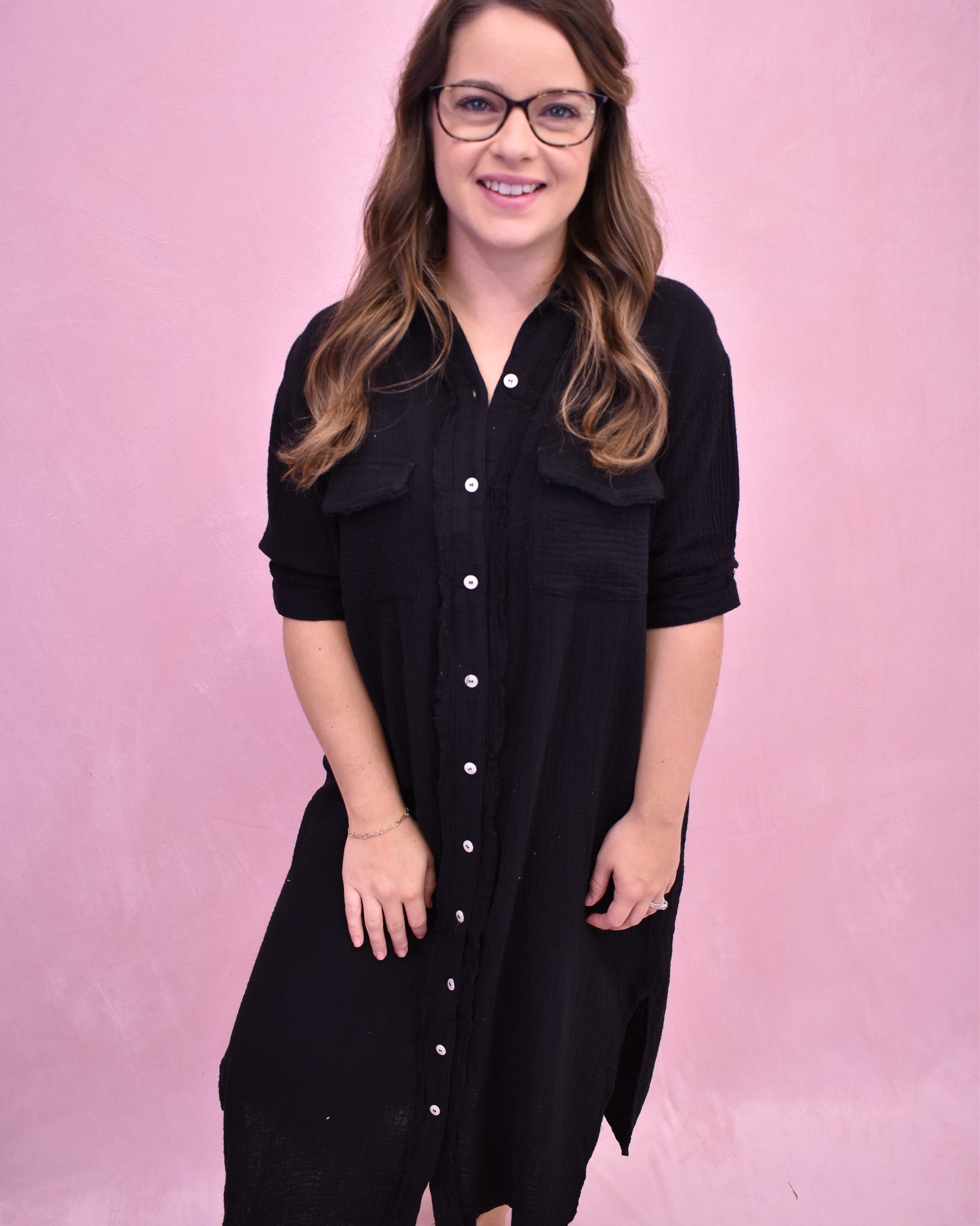 Woman wearing a black dress with white buttons against a pink background