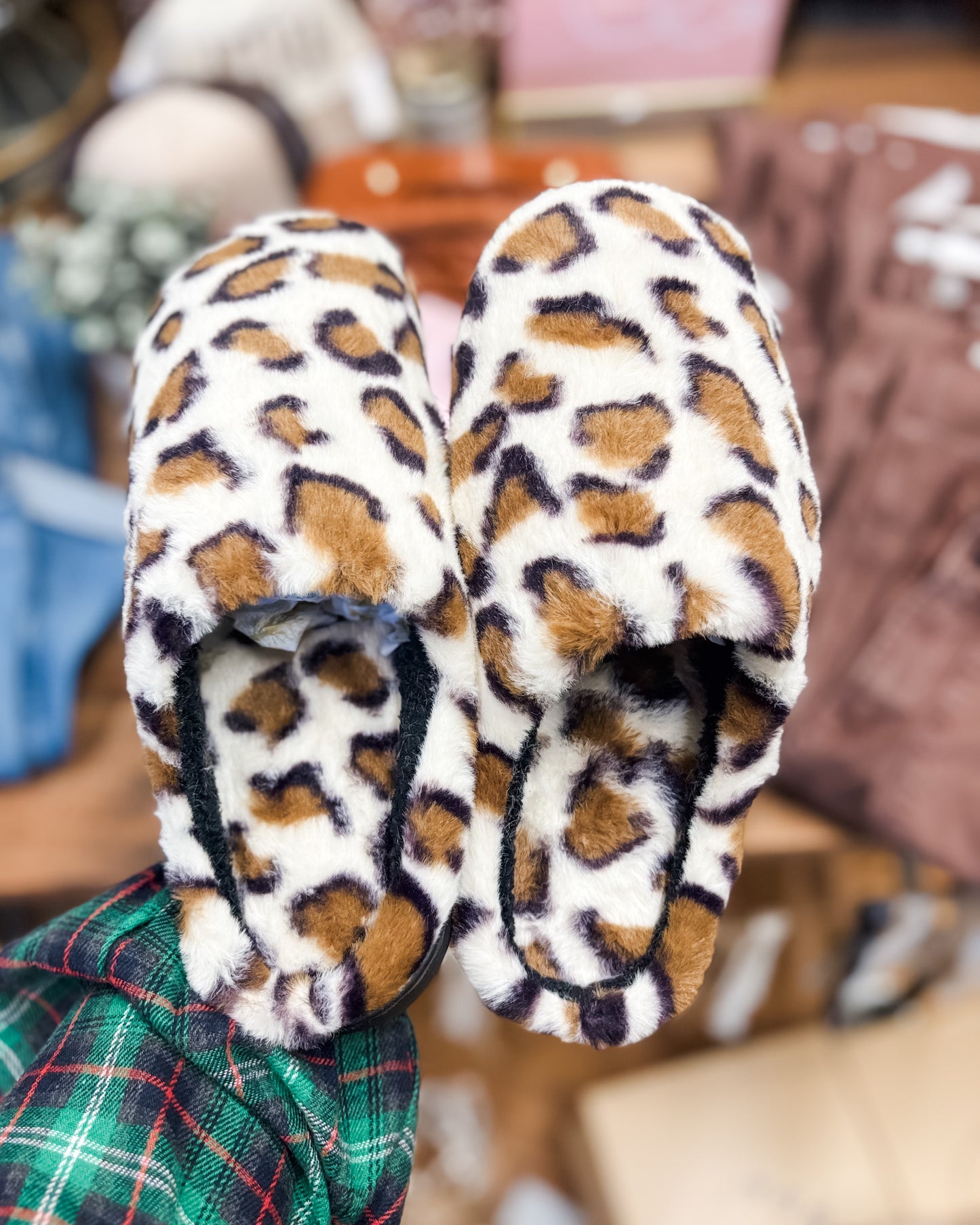 Pair of leopard print slippers held by a person wearing a plaid shirt.