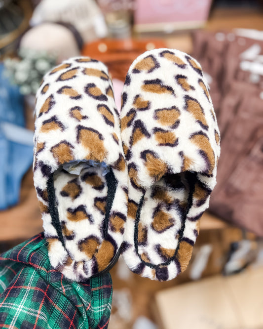 Pair of leopard print slippers held by a person wearing a plaid shirt.