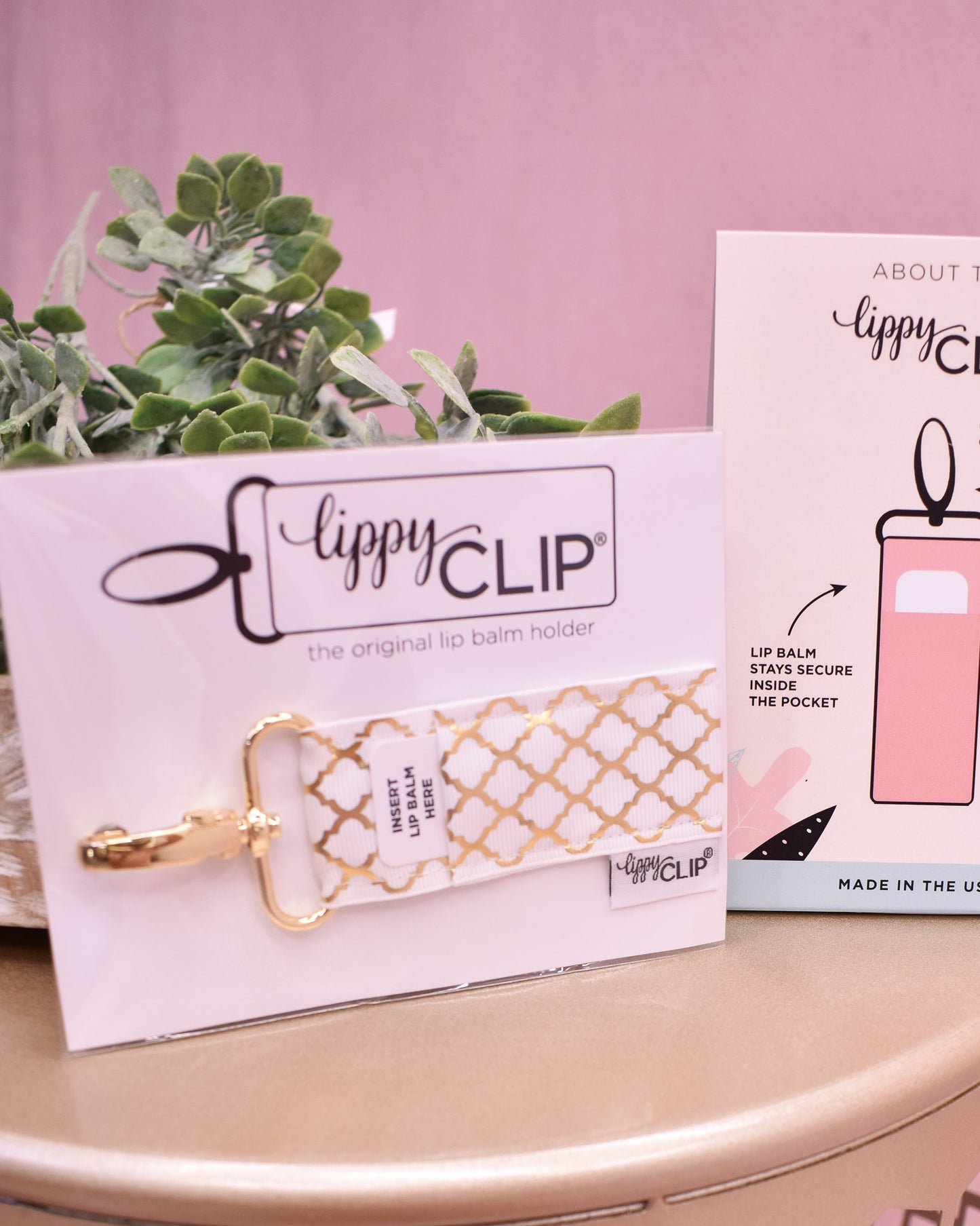 Gold lip balm holder with 'lippyCLIP' branding on a pink background