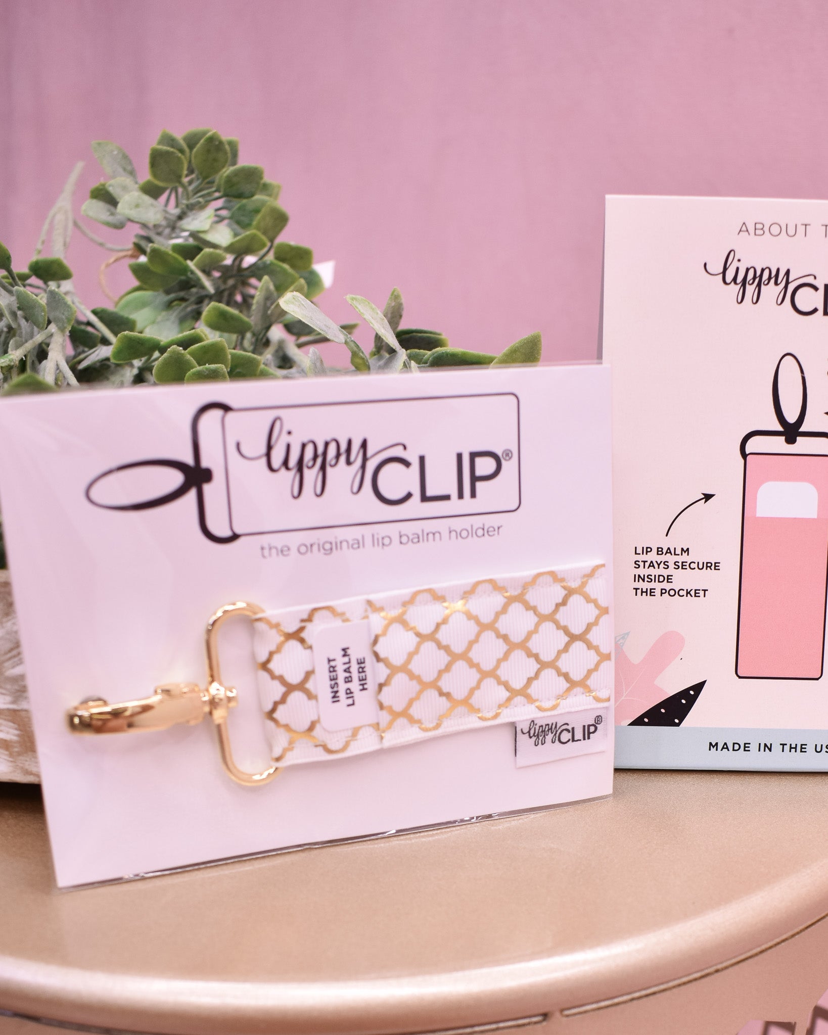 Gold lip balm holder with 'lippyCLIP' branding on a pink background