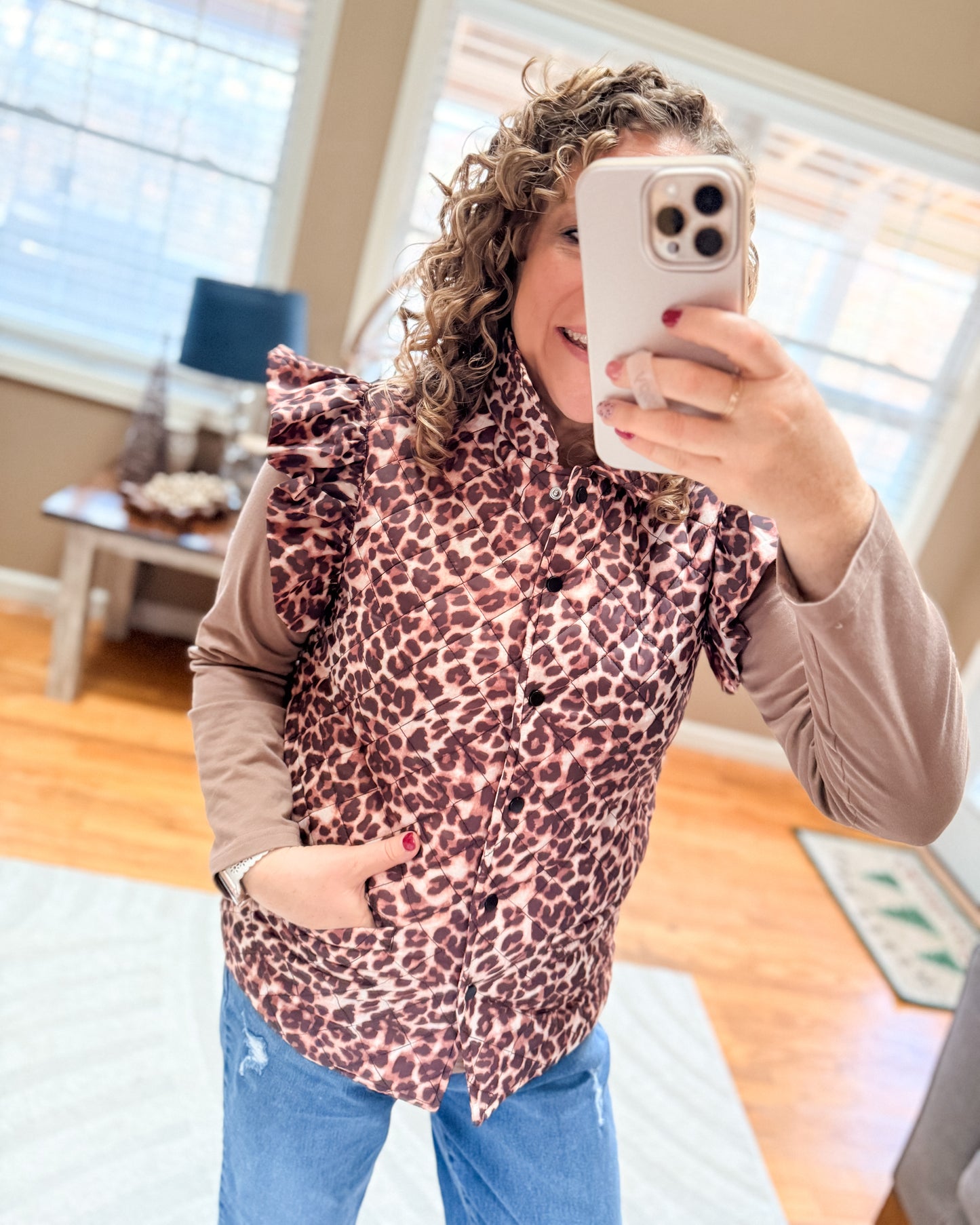 Person wearing a leopard print top and blue jeans, taking a mirror selfie.