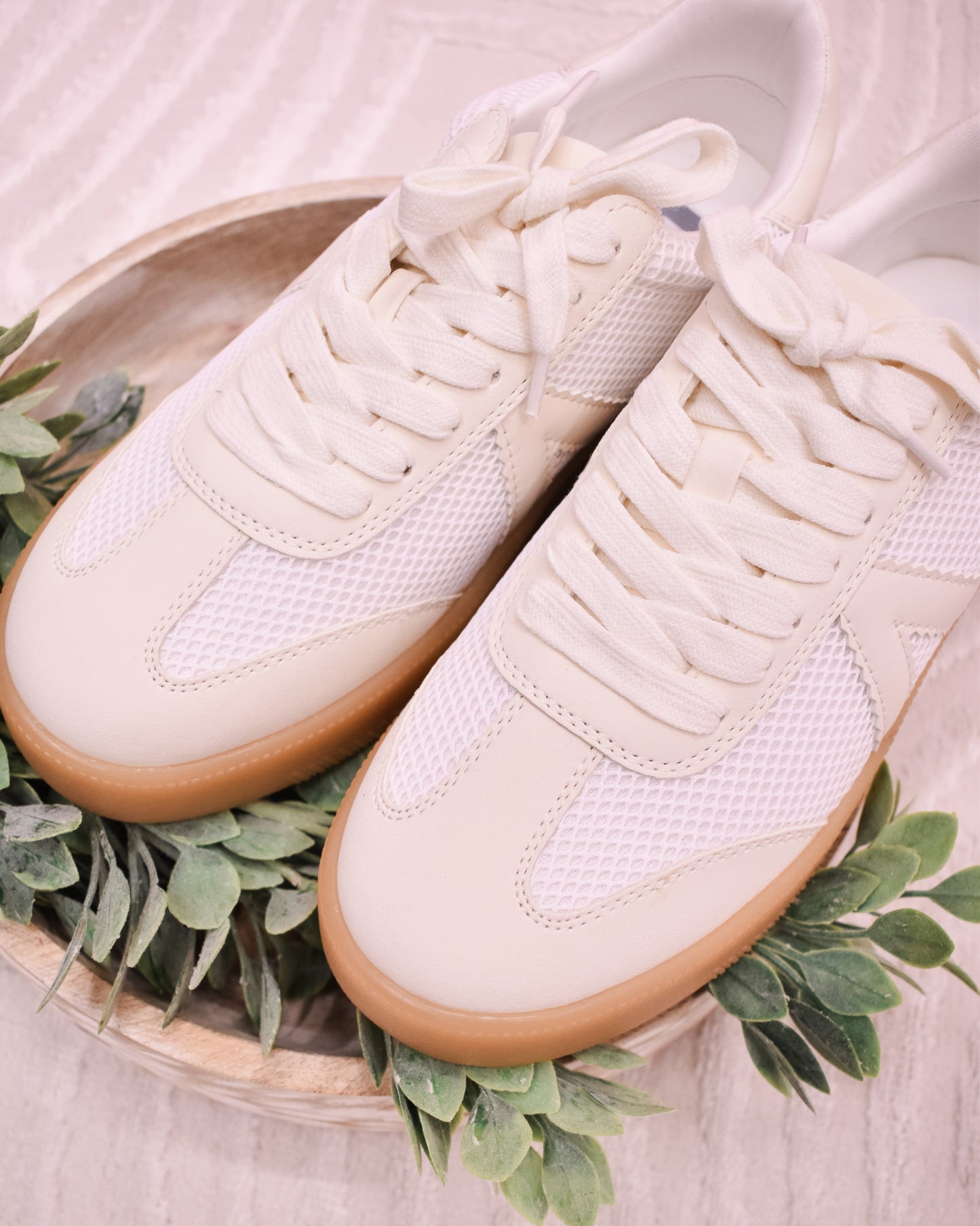 Pair of white sneakers with brown soles on a light background