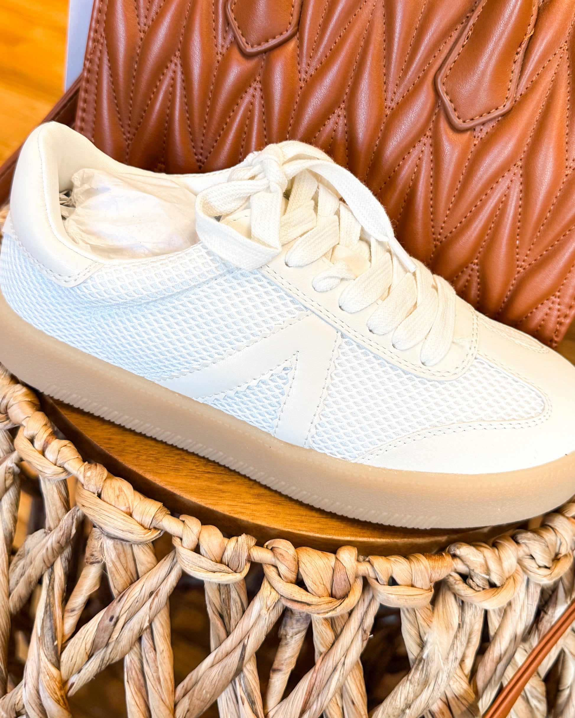 White sneakers on a woven surface with a brown leather bag in the background