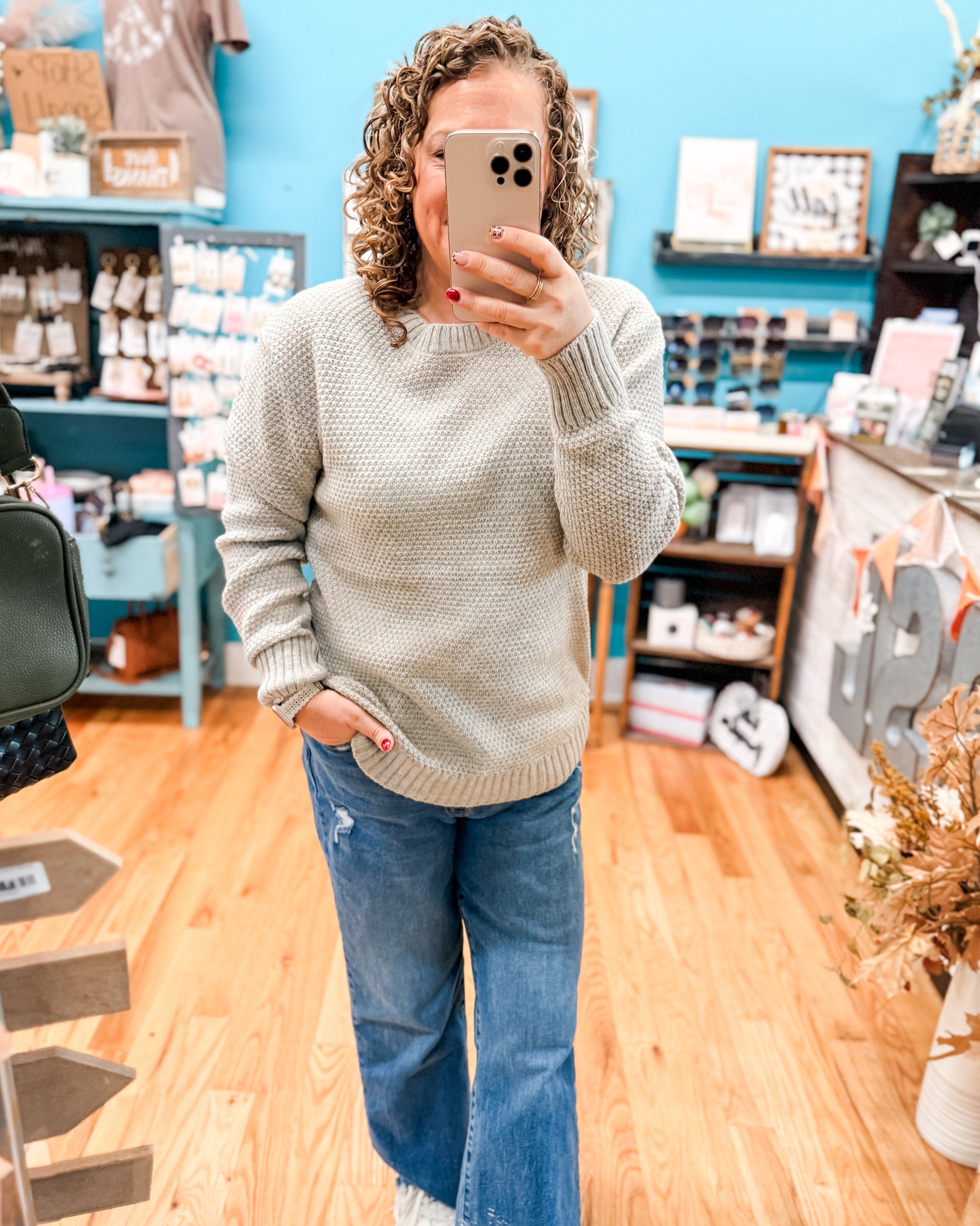 Person wearing a beige sweater and blue jeans taking a mirror selfie in a store.