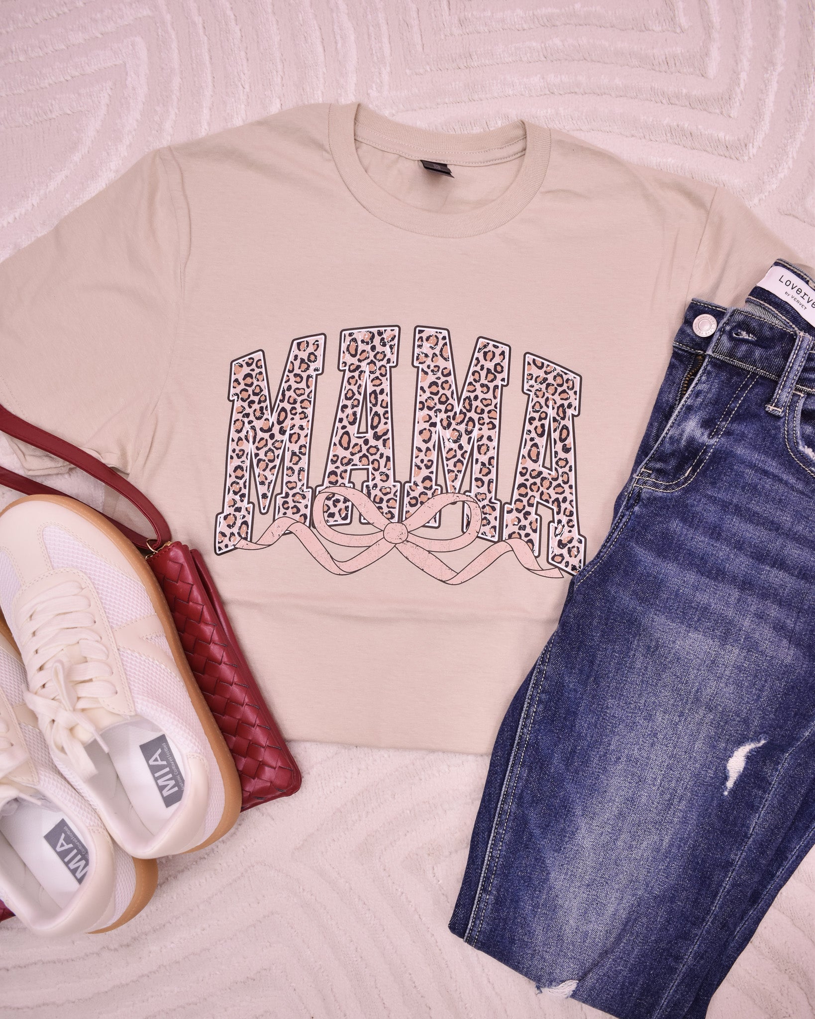 Beige t-shirt with leopard print design, blue jeans, white sneakers, and red handbag on a light background