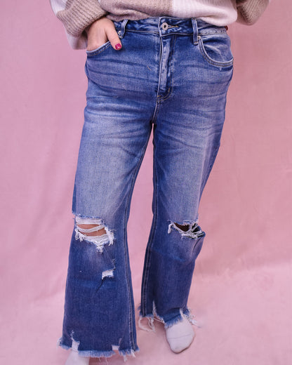 Person wearing blue flared jeans with a pink background