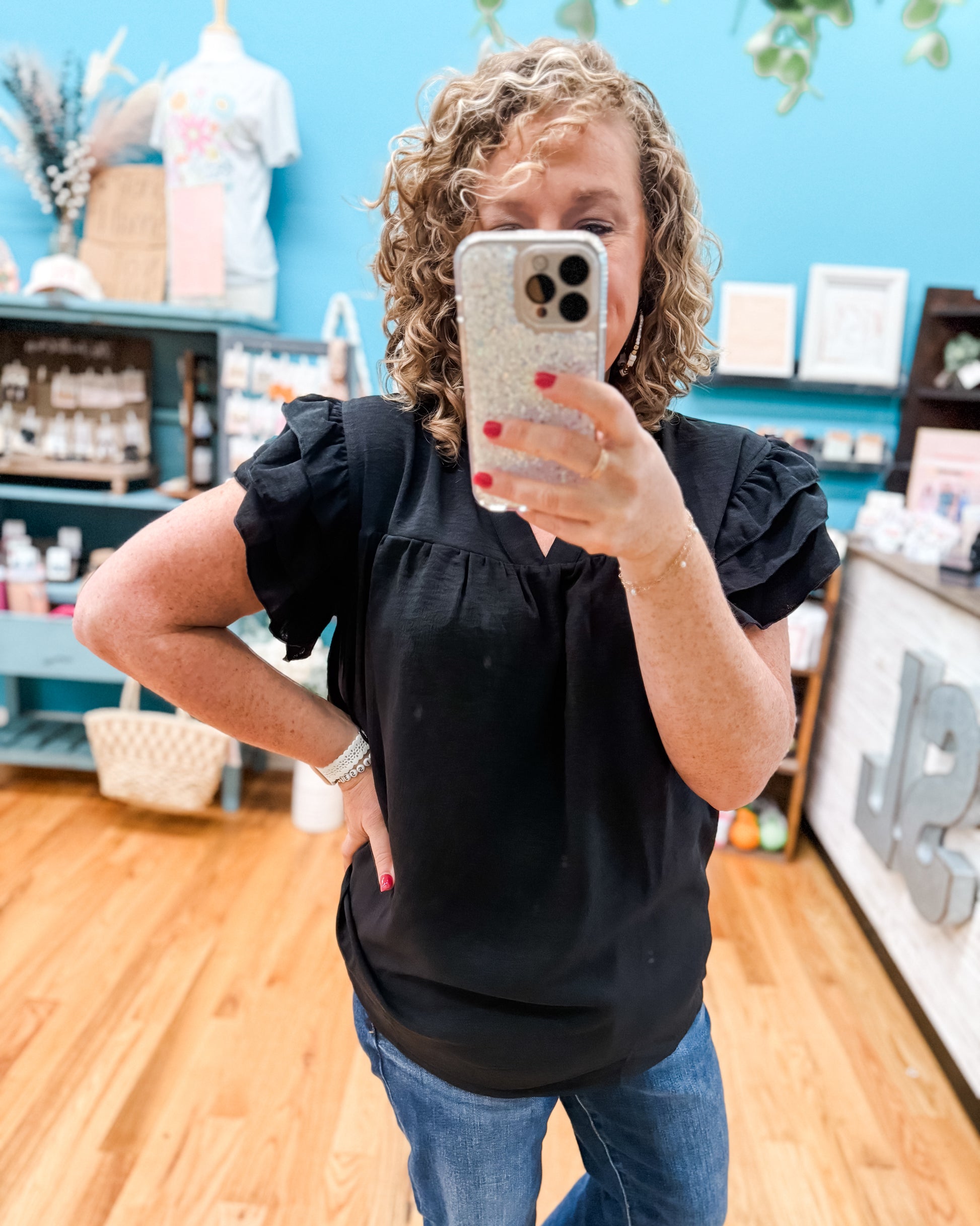 Person taking a mirror selfie wearing a black top and blue jeans in a store setting.