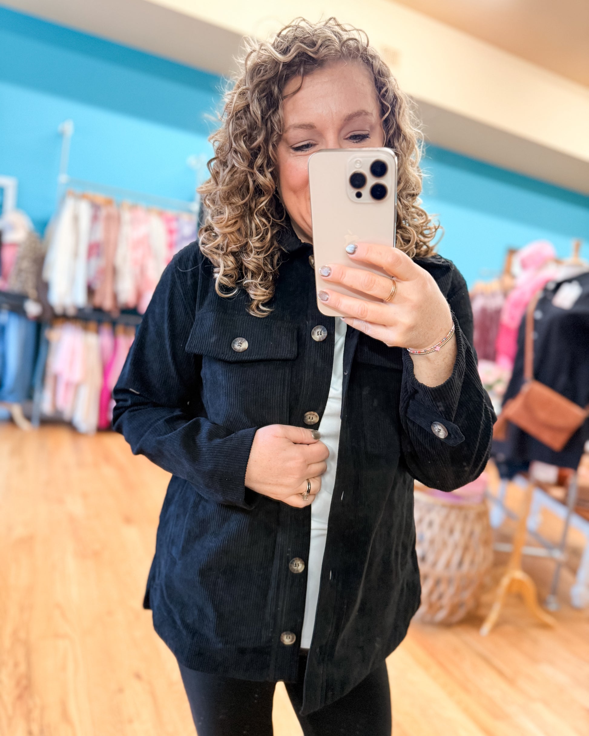 Person taking a mirror selfie wearing a black jacket in a store setting.
