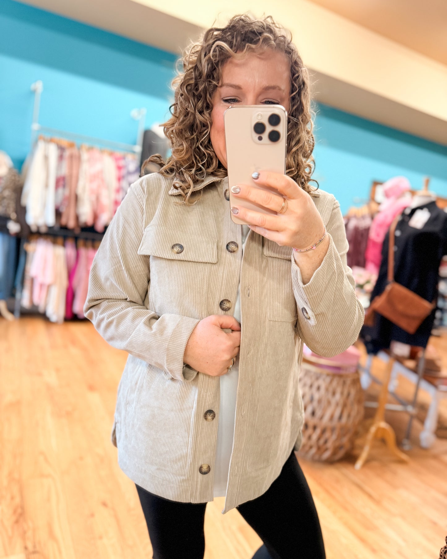 Person wearing a beige jacket taking a mirror selfie in a clothing store.