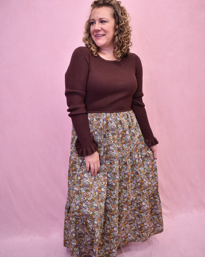 Woman wearing a brown sweater and floral skirt against a pink background