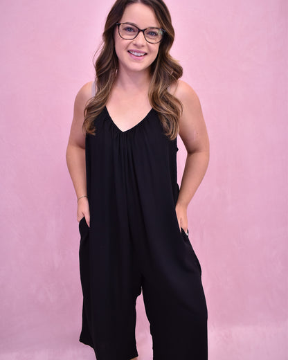 Woman wearing a black sleeveless jumpsuit against a pink background