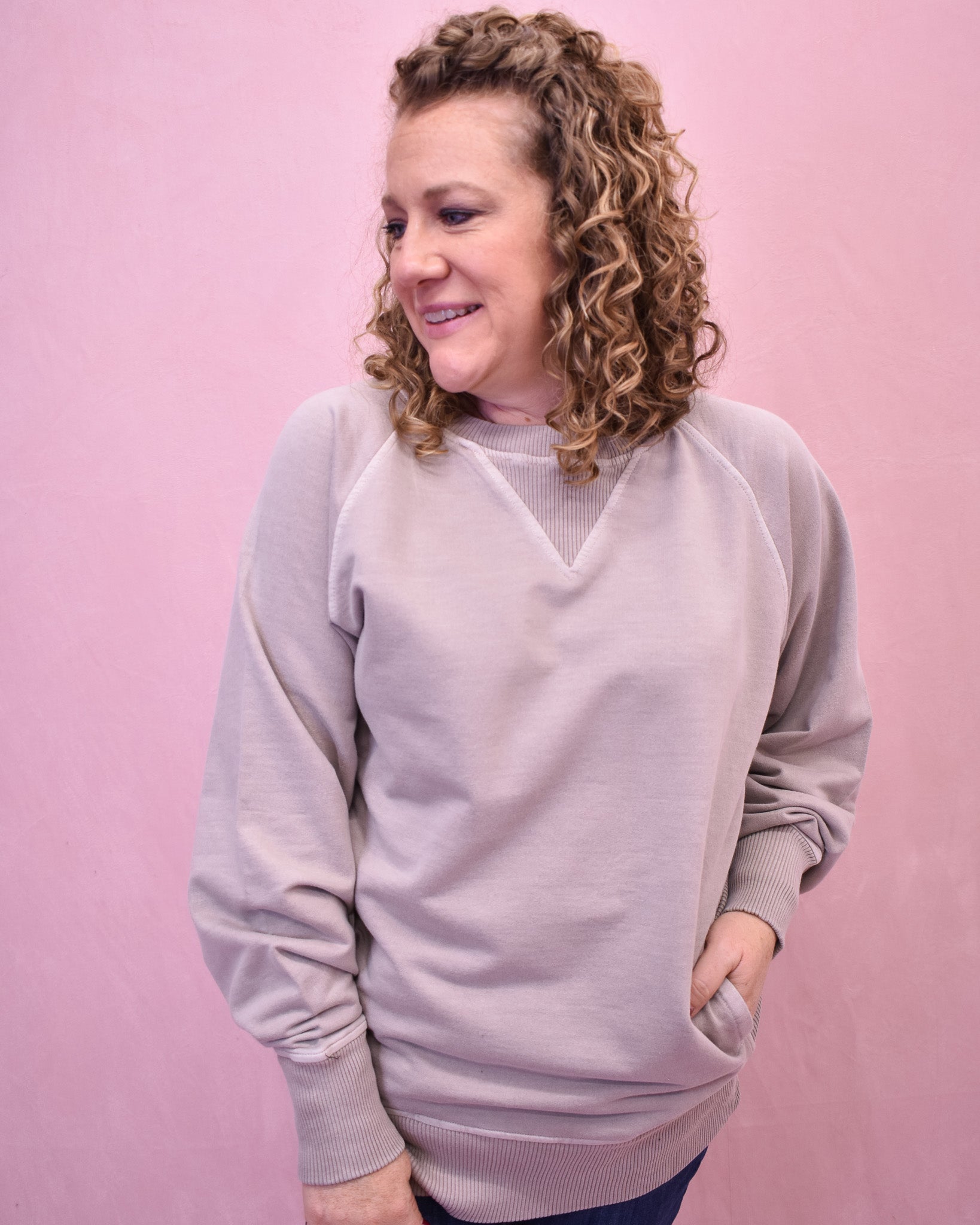 Woman wearing a light gray sweatshirt against a pink background
