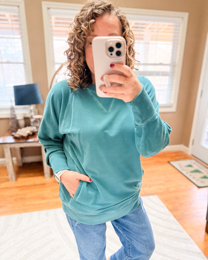 Person wearing a teal sweatshirt and blue jeans taking a mirror selfie.