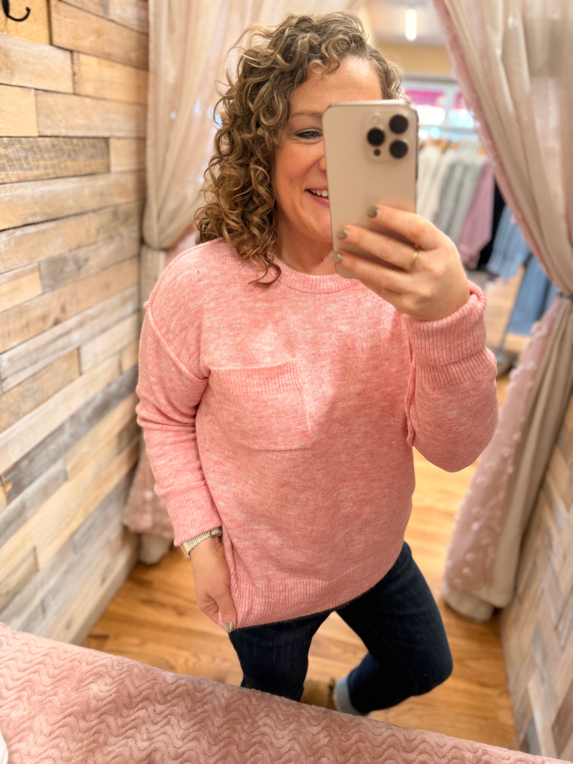 Person wearing a pink sweater taking a mirror selfie in a store.