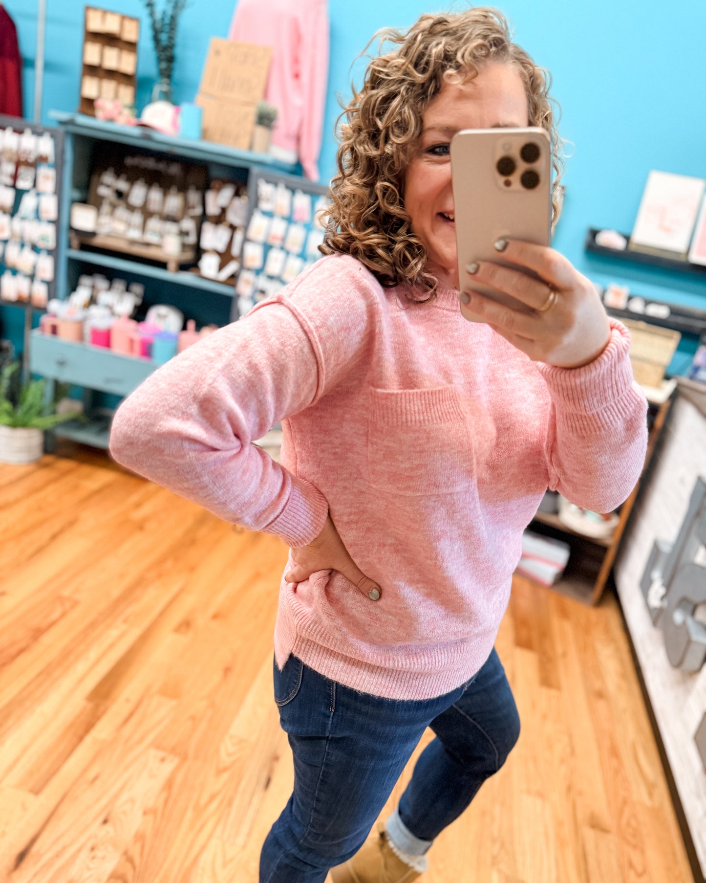 Woman in a pink sweater taking a mirror selfie in a store.