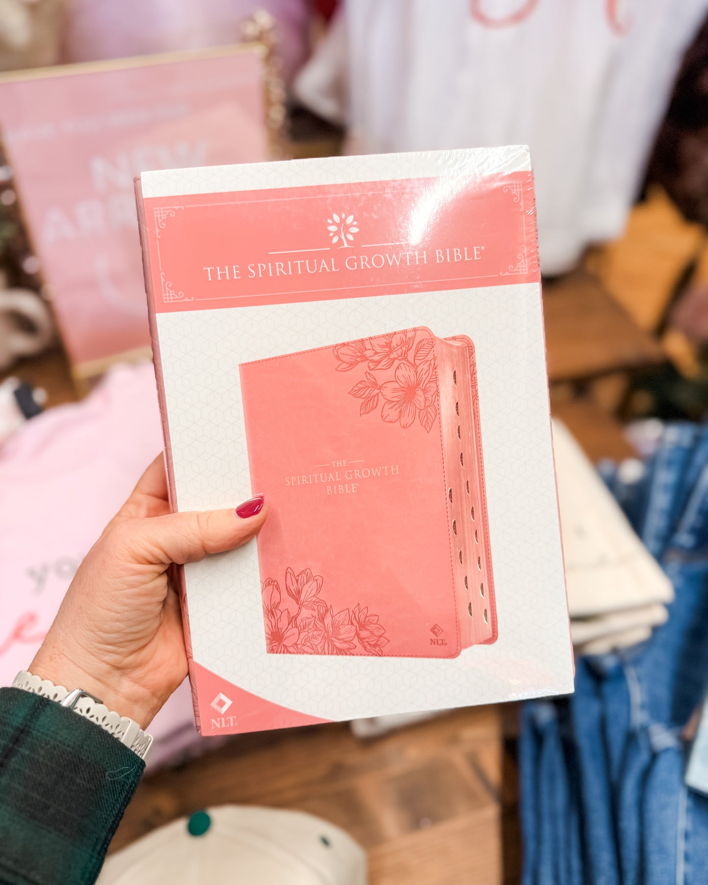Pink book titled 'The Spiritual Growth Bible' held by a person in a store setting.