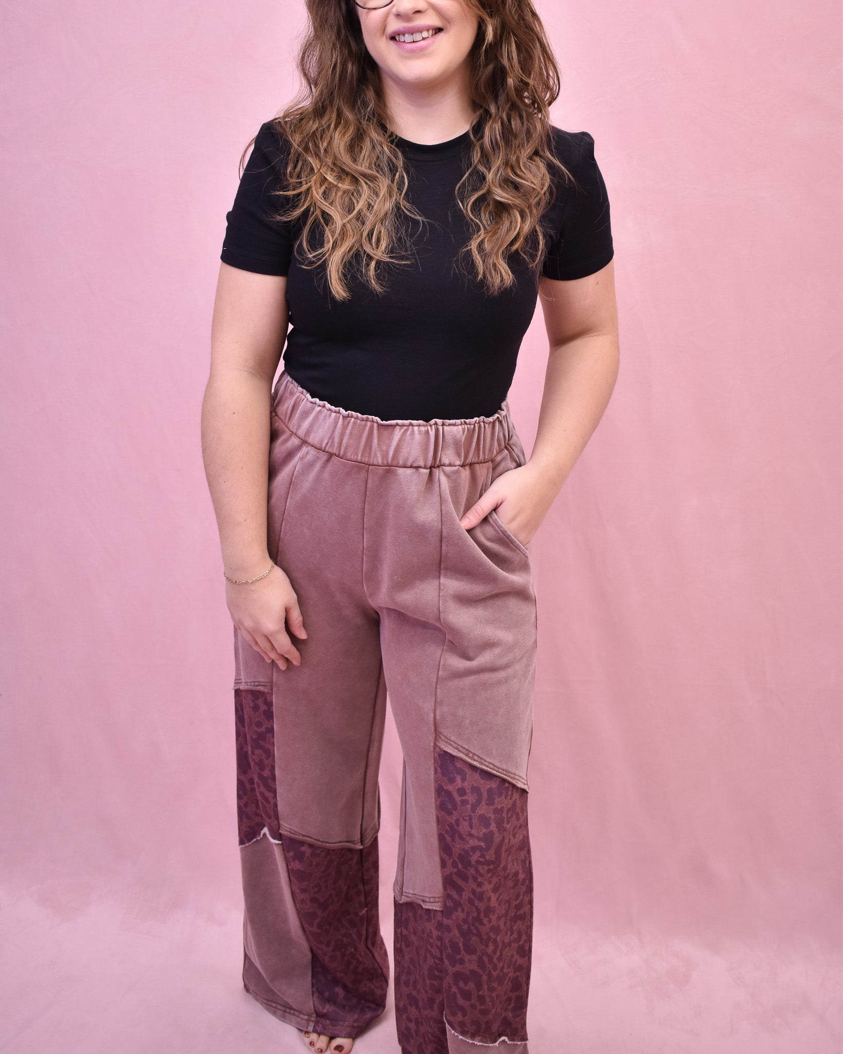 Woman wearing a black top and pink and purple patterned pants against a pink background