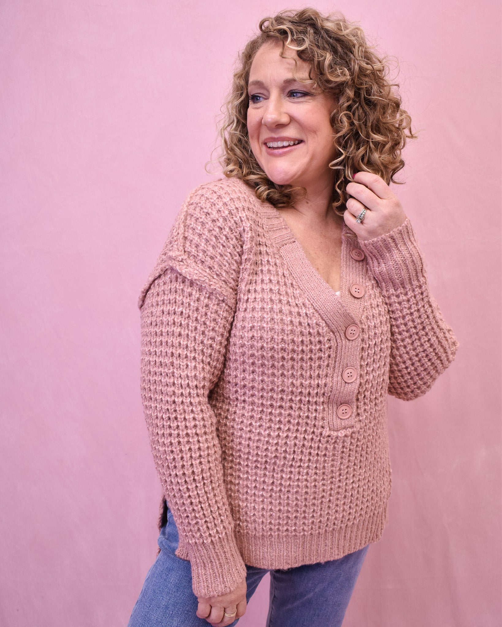 Woman wearing a pink knitted cardigan against a pink background