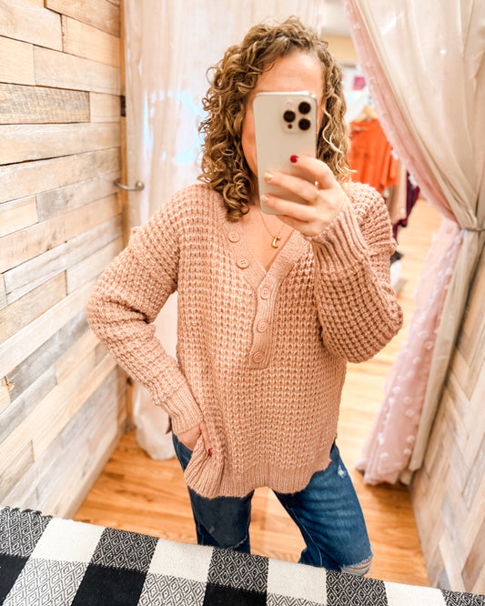 Person wearing a pink sweater taking a mirror selfie in a store.