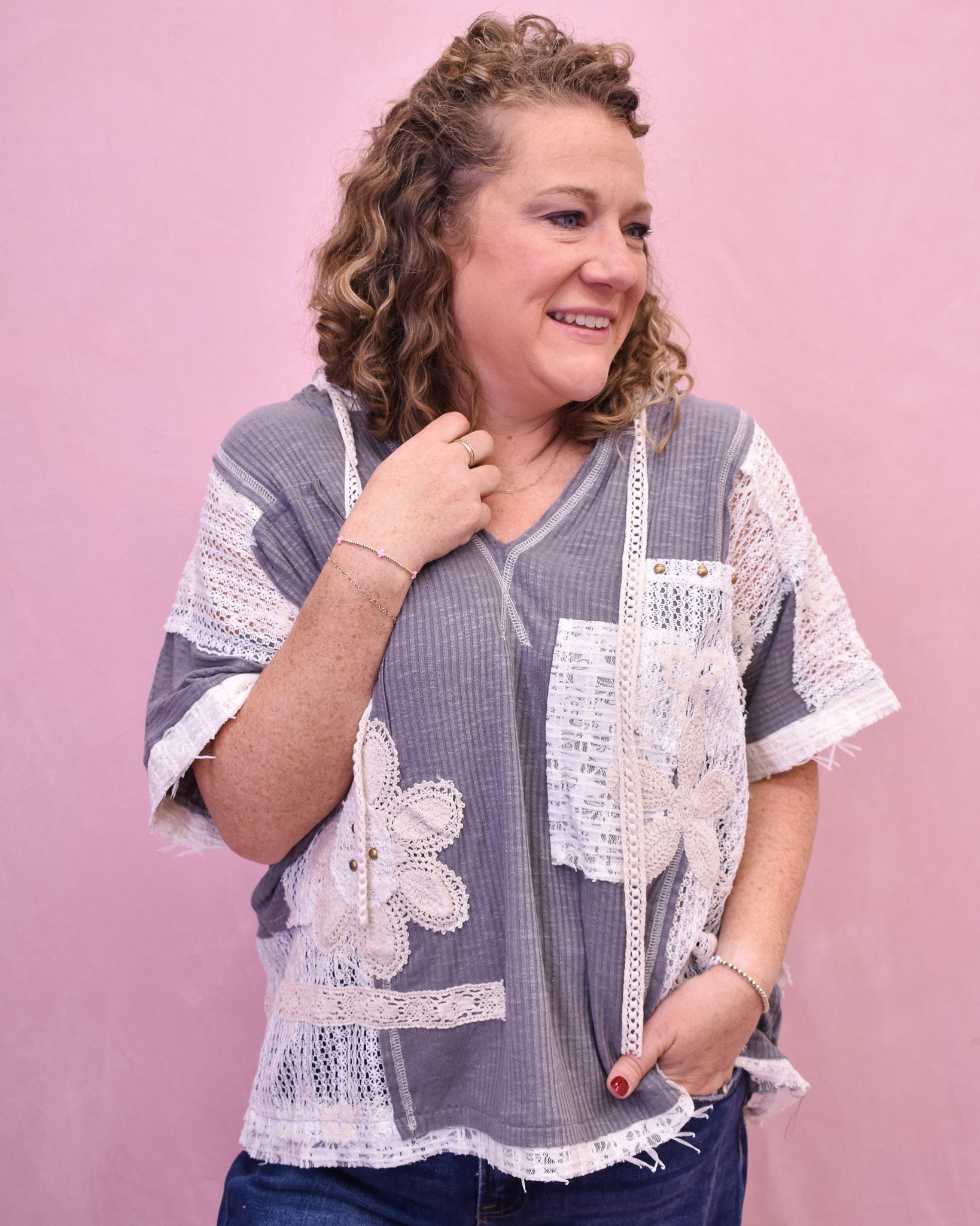 Woman wearing a gray and white lace-trimmed top against a pink background