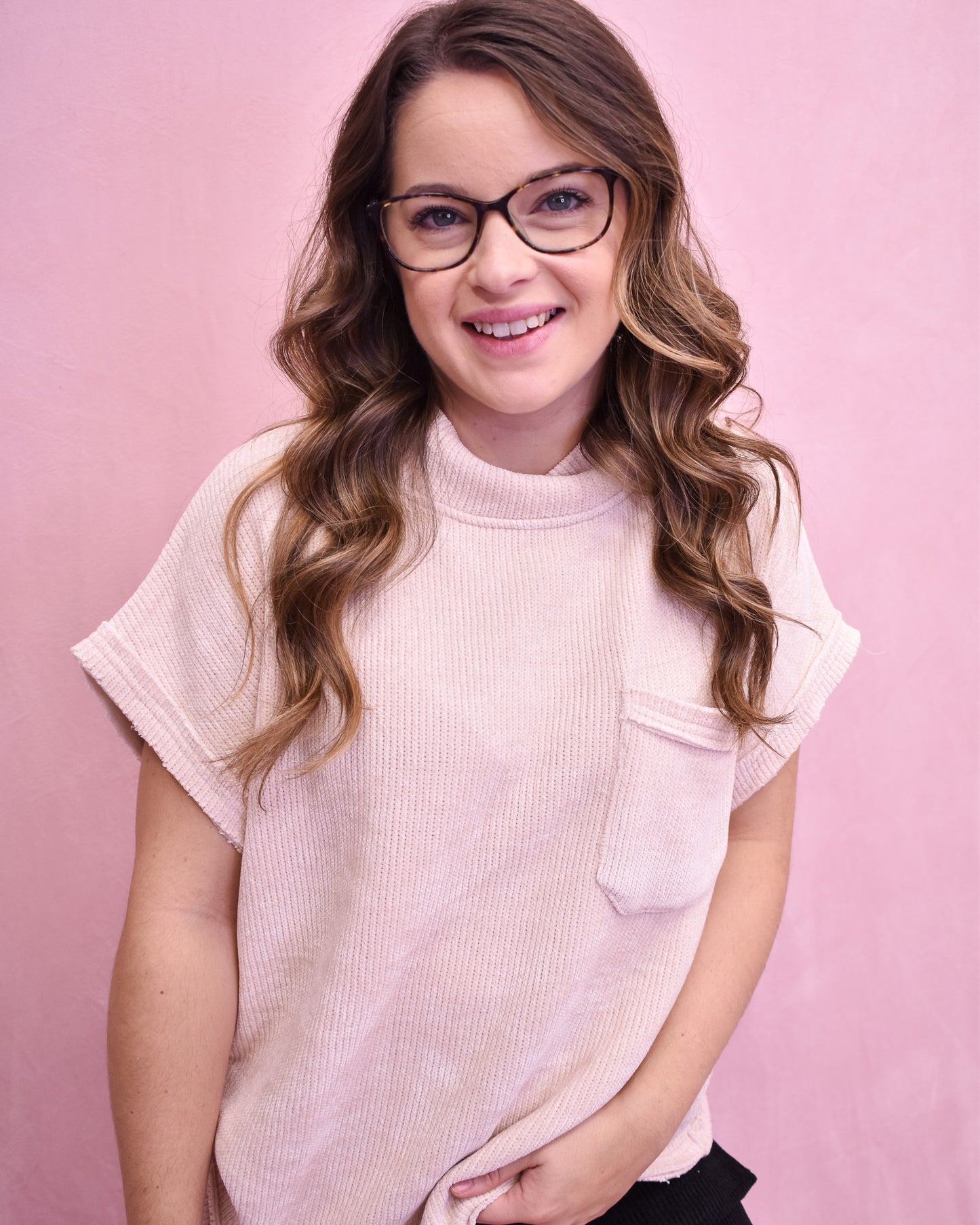 Woman wearing glasses and a light pink sleeveless top against a pink background