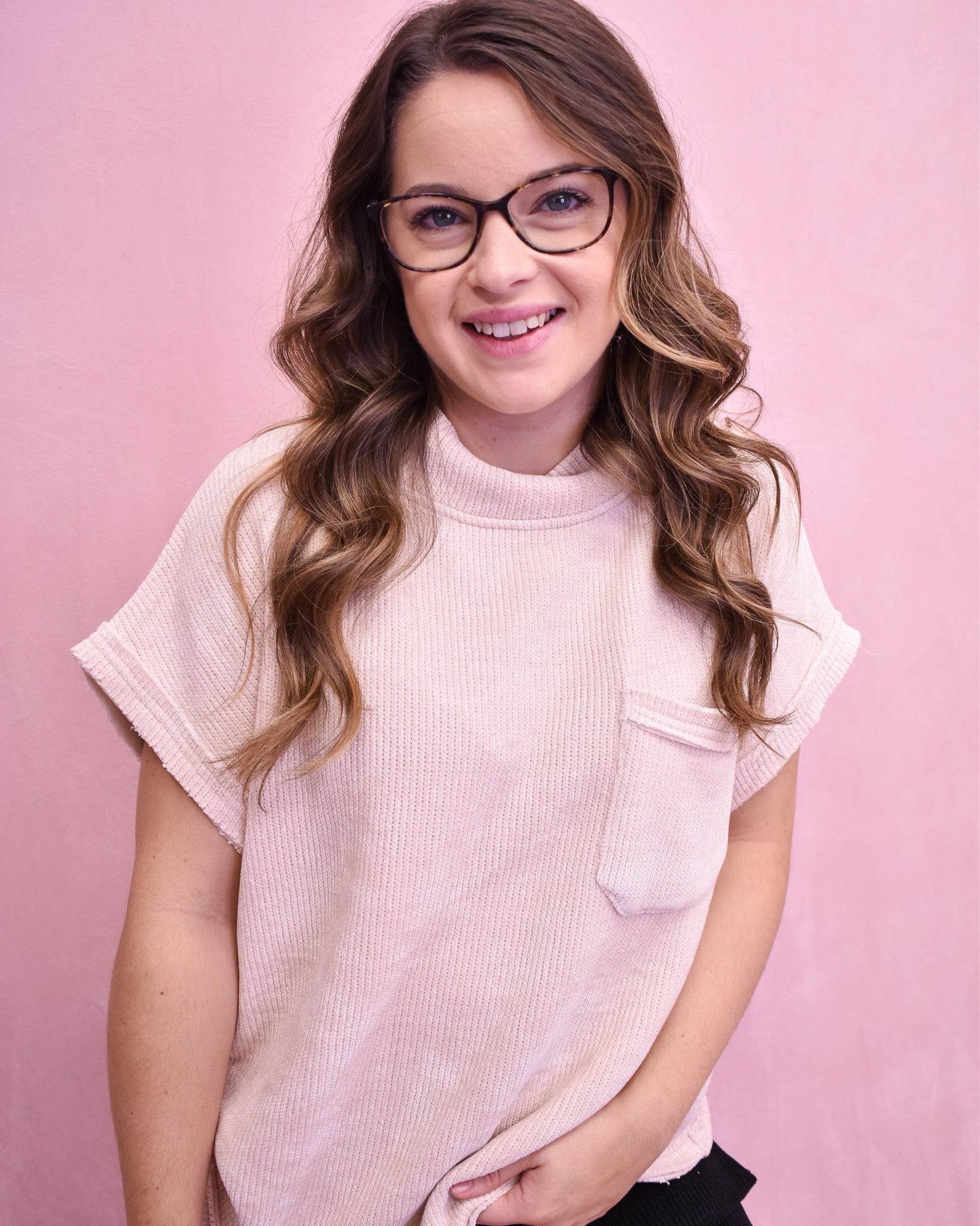 Woman wearing glasses and a light pink sleeveless top against a pink background