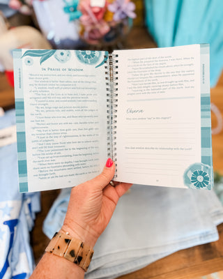 Hand holding an open spiral-bound book with decorative pages.