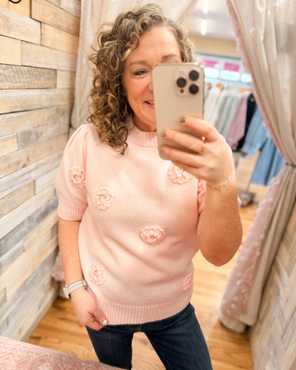 Woman taking a mirror selfie wearing a pink sweater with floral patterns in a store.
